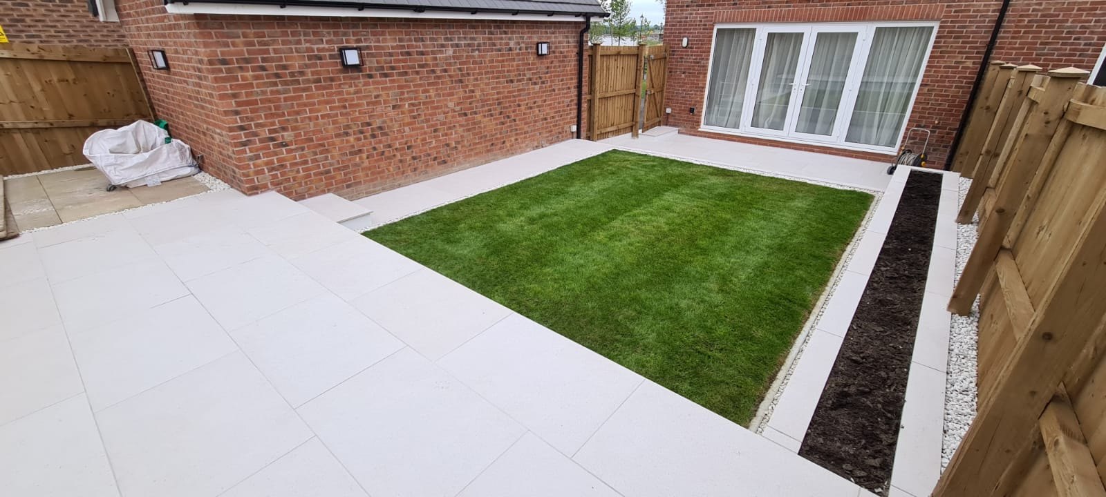 Finished new-build garden with porcelain patio, rendered walls and turf